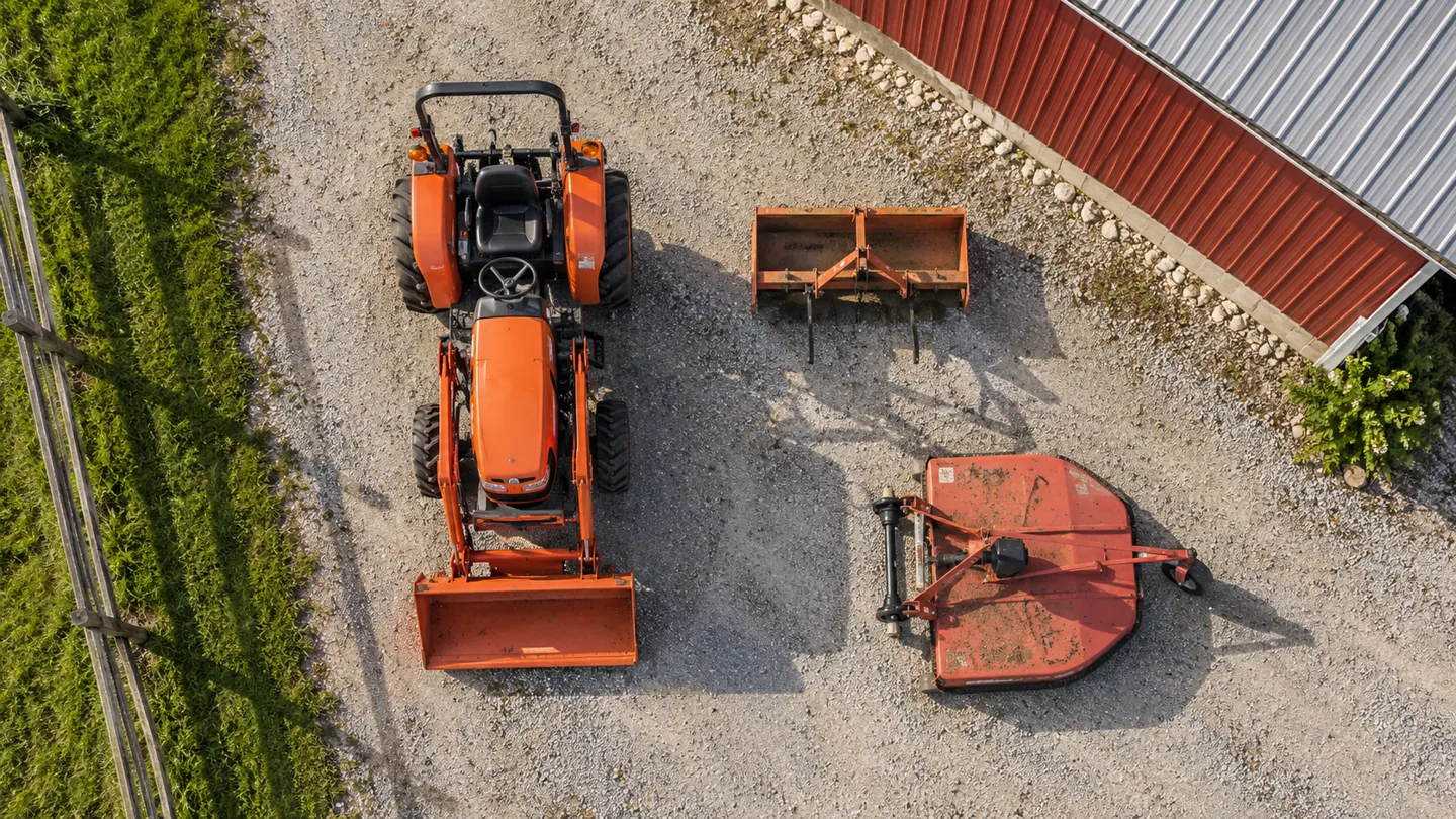 Compact tractor with front loader and implements parked on a small farm